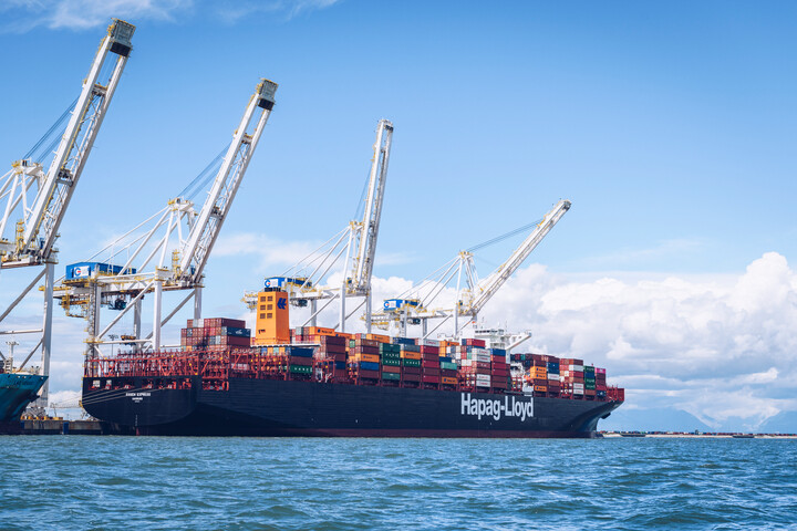 A shipping boat sitting at dock with four cranes above.
